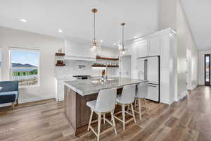 Kitchen with open shelves, hanging light fixtures, high end white refrigerator, tasteful backsplash, and a kitchen island with sink