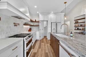 Kitchen with open shelves, high quality appliances, light stone counters, light wood-style flooring, and white cabinets