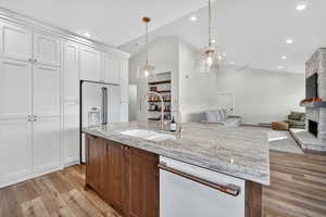 Kitchen featuring white cabinets, white appliances, light wood-type flooring, a center island with sink, and recessed lighting