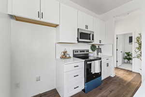 Kitchen with appliances with stainless steel finishes, white cabinets, dark wood-type flooring, and decorative backsplash