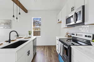 Kitchen featuring appliances with stainless steel finishes, white cabinets, decorative light fixtures, dark wood-style floors, and beamed ceiling