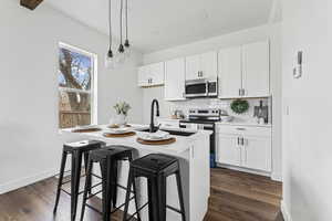 Kitchen with a kitchen bar, white cabinetry, appliances with stainless steel finishes, pendant lighting, and recessed lighting