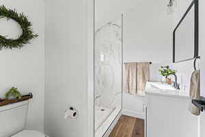 Full bathroom with vanity, a marble finish shower, and dark wood-type flooring
