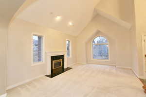 Unfurnished living room with light colored carpet, high vaulted ceiling, a tiled fireplace, and arched walkways