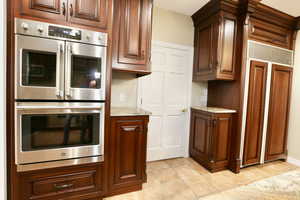 Kitchen with stainless steel double oven, granite counters, paneled built in Sub-Zero refrigerator, and light tile patterned flooring