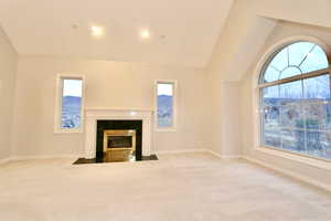 Unfurnished living room with vaulted ceiling, carpet flooring, and a fireplace with flush hearth