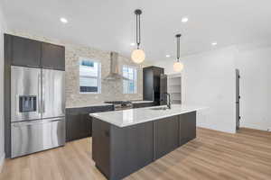 Kitchen with appliances with stainless steel finishes, tasteful backsplash, pendant lighting, recessed lighting, and wall chimney range hood