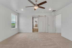 Unfurnished bedroom featuring a barn door, ceiling fan, light carpet, and recessed lighting