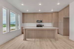 Kitchen with modern cabinets, appliances with stainless steel finishes, a kitchen island with sink, light stone countertops, and a mountain view