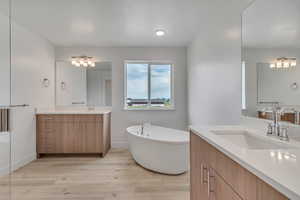 Full bathroom with a soaking tub, two vanities, and light wood finished floors