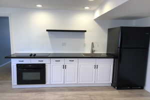 Kitchen with dark countertops, black appliances, white cabinets, light wood finished floors, and recessed lighting