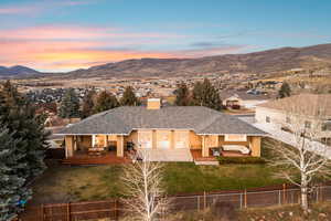 Back of house at dusk featuring a chimney, a shingled roof, a fenced backyard, and a deck with mountain view