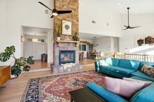 Living area with ceiling fan, light wood-style floors, a high ceiling, and a stone fireplace