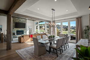 Dining space with a stone fireplace, a chandelier, a raised ceiling, wood finished floors, and recessed lighting