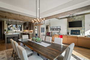 Dining space with beamed ceiling, dark wood-style flooring, plenty of natural light, and a stone fireplace