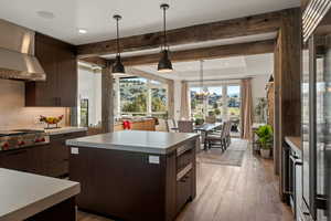 Kitchen featuring dark brown cabinetry, beam ceiling, pendant lighting, light wood finished floors, and wall chimney exhaust hood