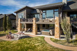 Rear view of house featuring a patio area, stone siding, an outdoor fire pit, and a chimney