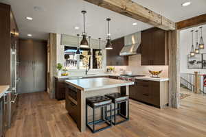 Kitchen with decorative light fixtures, a breakfast bar, modern cabinets, recessed lighting, and wall chimney exhaust hood