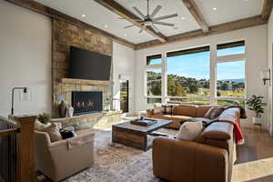 Living area featuring wood finished floors, a stone fireplace, ceiling fan, beam ceiling, and recessed lighting