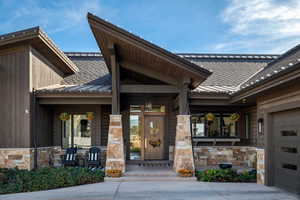 Entrance to property with stone siding, an attached garage, roof with shingles, and a porch