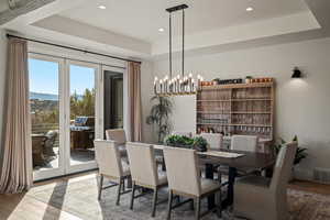 Dining area featuring a tray ceiling, light wood-style flooring, a chandelier, recessed lighting, and a water view