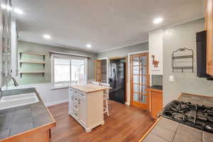 Kitchen with a wainscoted wall, black fridge, light wood-type flooring, range with gas cooktop, and tile counters