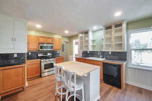 Kitchen featuring a kitchen bar, decorative backsplash, appliances with stainless steel finishes, glass insert cabinets, and recessed lighting