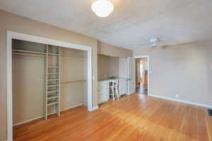 bedroom featuring a textured ceiling, light wood-style floors, a closet, an office area, and ceiling fan