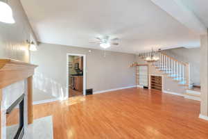 living room featuring a fireplace, light wood-style floors, a chandelier, a ceiling fan, and stairs