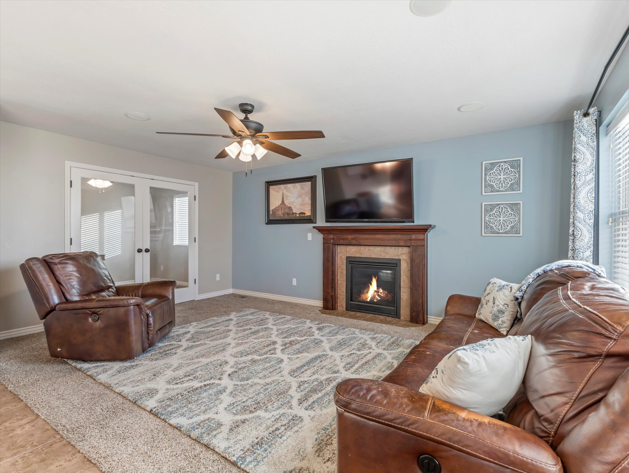 Carpeted living room with a fireplace with flush hearth, french doors, and a ceiling fan