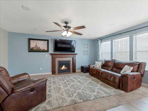 Living area featuring a tiled fireplace, ceiling fan, light colored carpet, and light tile patterned floors