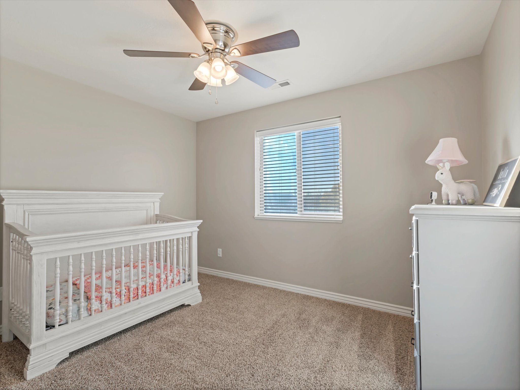 Bedroom featuring light colored carpet, ceiling fan, and a nursery area