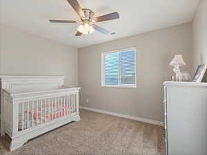 Bedroom featuring light colored carpet, ceiling fan, and a nursery area