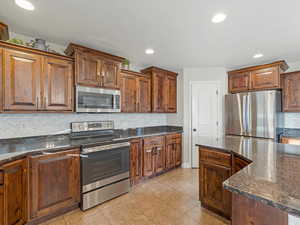 Kitchen featuring stainless steel appliances, dark stone countertops, recessed lighting, decorative backsplash, and light tile patterned floors