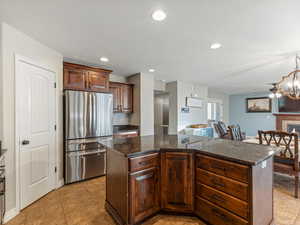 Kitchen with freestanding refrigerator, a kitchen island, a glass covered fireplace, dark stone counters, and recessed lighting