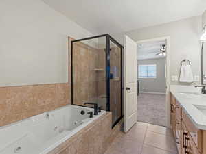Master Suite bathroom with double vanity, a tub with jets, a shower stall, light tile patterned floors, and a ceiling fan