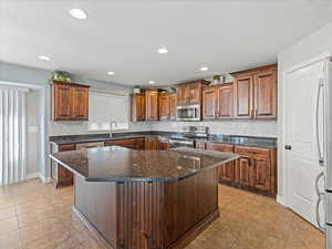 Kitchen with dark stone countertops, stainless steel appliances, a center island, backsplash, and recessed lighting
