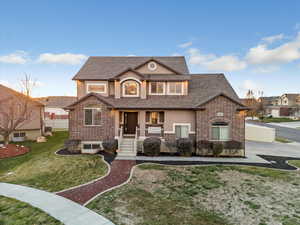View of front of home with covered porch, brick siding, a shingled roof, and stucco siding