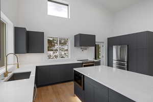 Kitchen with modern cabinets, light stone countertops, a towering ceiling, appliances with stainless steel finishes, and gray cabinets