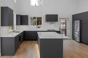 Kitchen featuring light stone counters, a towering ceiling, modern cabinets, a kitchen island, and stainless steel appliances