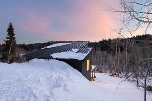 View of snow covered exterior featuring a metal roof and a wooded view