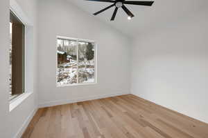 Empty room with vaulted ceiling, light wood finished floors, and ceiling fan