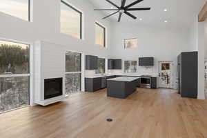 Living area with a large fireplace, light wood-type flooring, ceiling fan, a high ceiling, and recessed lighting