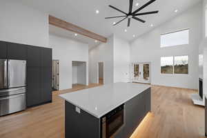 Kitchen with dark cabinetry, high vaulted ceiling, a fireplace with raised hearth, a kitchen island, and appliances with stainless steel finishes