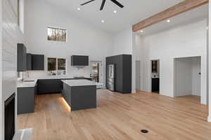 Kitchen with high vaulted ceiling, a center island, light wood finished floors, freestanding refrigerator, and dark cabinets