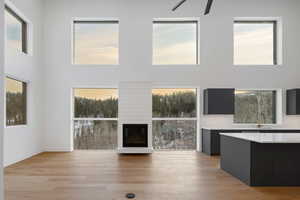 Unfurnished living room with a high ceiling, light wood-style floors, a large fireplace, and a ceiling fan