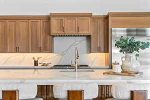 Kitchen featuring built in refrigerator, brown cabinetry, light stone countertops, and a kitchen bar