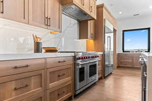 Kitchen with high quality appliances, light wood-style flooring, under cabinet range hood, recessed lighting, and light stone countertops