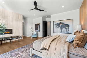 Bedroom featuring a glass covered fireplace, wood finished floors, ceiling fan, recessed lighting, and wooden walls