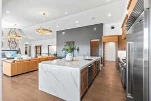 Kitchen featuring high quality appliances, light stone counters, brown cabinets, open floor plan, and recessed lighting